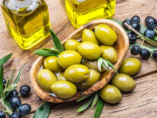 Оливковые ягоды и бутылка оливкового масла на деревянном столе . — стоковое фото