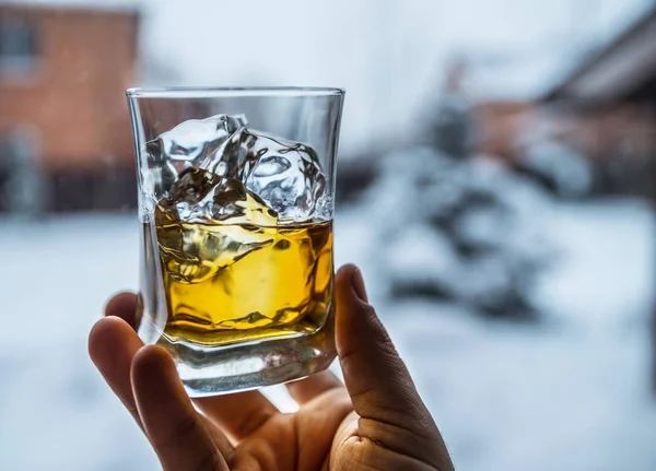 男の手に氷とウィスキーのグラス。冬の自然 — ストック写真