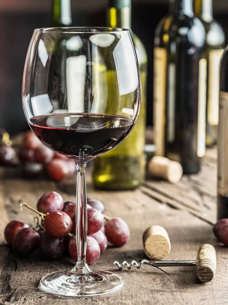 Una copa de vino tinto en la mesa. Botella de vino y uvas en la ba — Foto de Stock