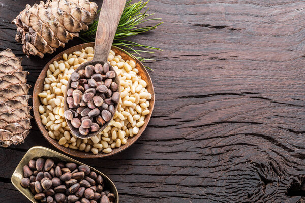 Pine nuts in the spoon and pine nut cone on the wooden table. Or