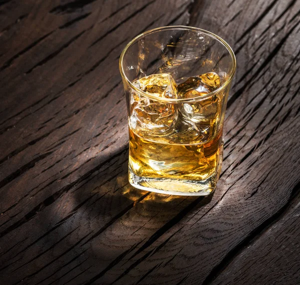 Whiskey glass or glass of whiskey with ice cubes on the wooden b
