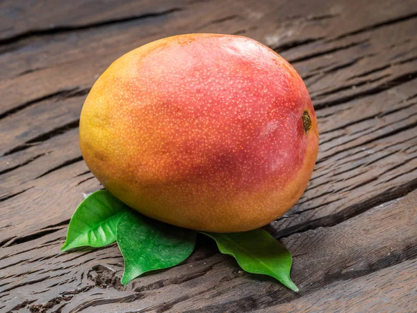 Ripe mango fruit with mango leaves on wooden background.