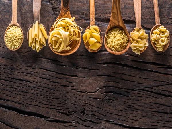 Diversi tipi di pasta in cucchiai di legno sul tavolo. Vista dall'alto. — Foto Stock