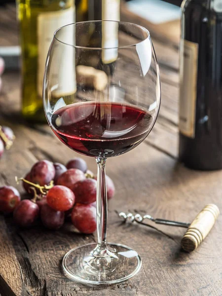 Una copa de vino tinto en la mesa. Botella de vino y uvas en la ba — Foto de Stock