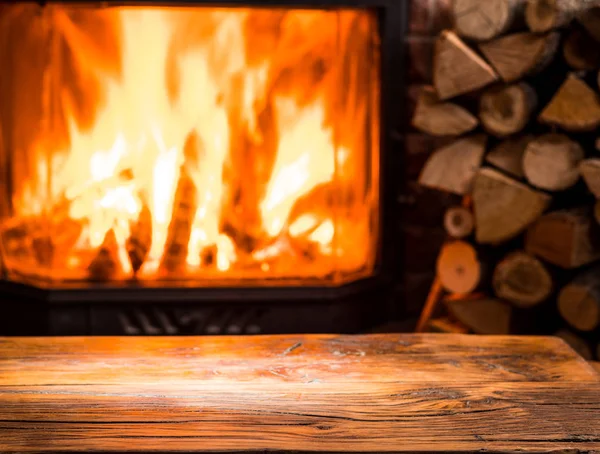 Starý dřevěný stůl a krb s teplým ohněm v pozadí. — Stock fotografie