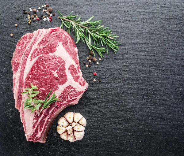 Rib eye steak with spices on the black background.