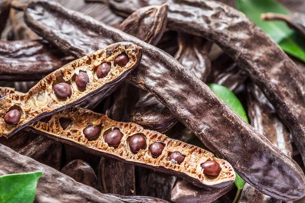 Carob pods and carob beans on the wooden table. — Stock Photo, Image