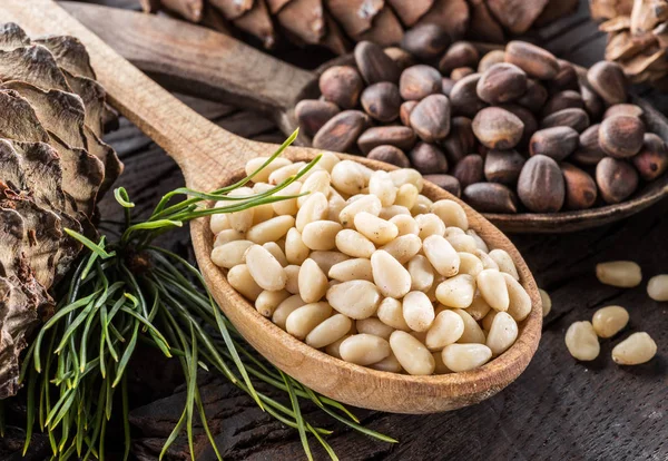 Pine nuts in the spoon and pine nut cone on the wooden table. Or — Stock Photo, Image