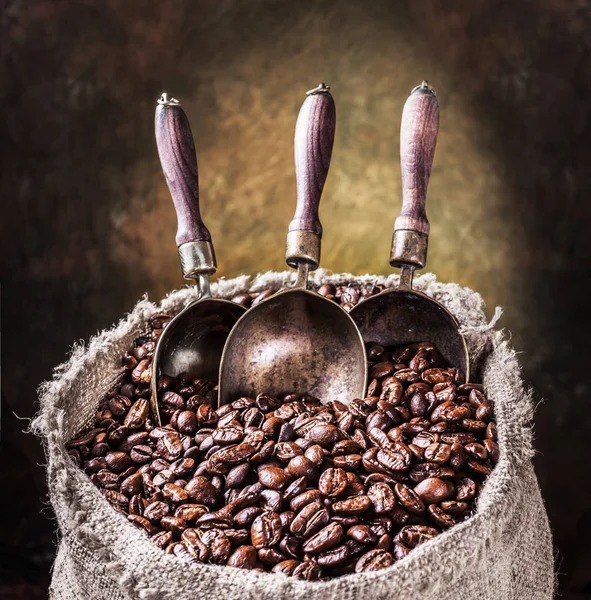 Granos de café tostados y cucharadas de cobre en el viejo saco. Bacs oscuro — Foto de Stock