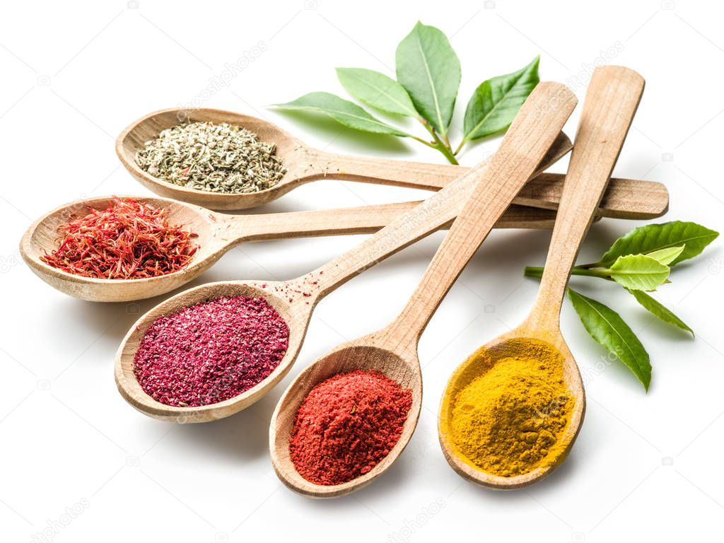 Assortment of colorful spices in the wooden spoons on the white 