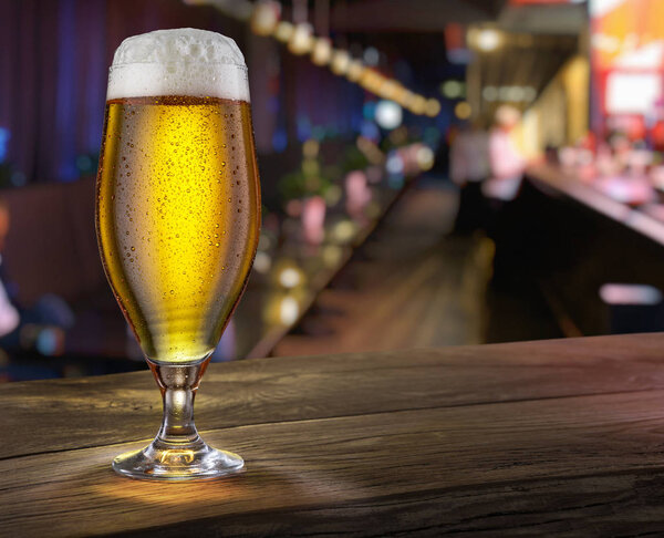 Frosty glass of light beer on the bar counter.