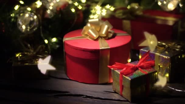 赤いギフトボックス付きのクリスマスの背景 カメラはゆっくりと贈り物に近づき前景と背景はクリスマスライトの美しいボケ — ストック動画