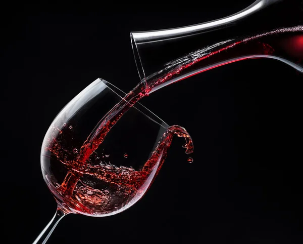 Red wine is poured into a wine glass on a black background. — Stock Photo, Image