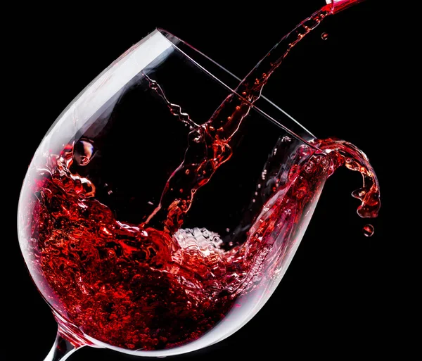 Il vino rosso viene versato in un bicchiere di vino su uno sfondo nero. — Foto Stock