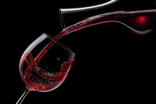 Il vino rosso viene versato in un bicchiere di vino su uno sfondo nero. — Foto Stock