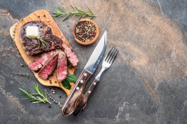 Otlar ve ahşap tepsi üzerinde tereyağı bir parça ile Orta nadir Ribeye biftek. Üstte görüntü.