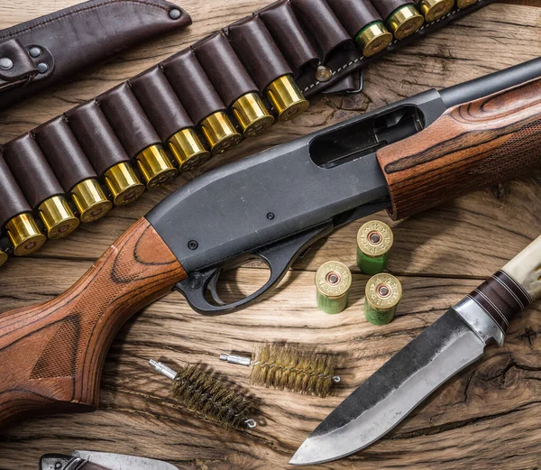 Hunting equipment - pump action shotgun,  12 guage cartridge and hunting knife on the wooden table.