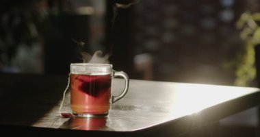 Sıcak çay bardağı odanın içindeki eski bir masanın üzerinde duruyor ve güneşin arka ışığında yavaş yavaş buhar yayıyor. Ağır çekim. Blackmagic Sineması Kamera 6K.