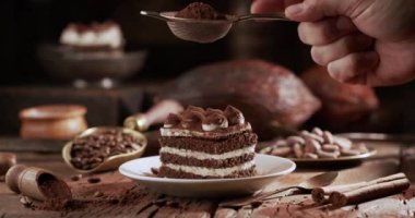 Tiramisu kekinin üzerine, aşçı süzgeçten yüzeye kakao serpiyor. Tatlılar ve eski mutfak gereçleri için malzemeler içeren karanlık bir arka plan. Ağır çekim, Kara Büyü Sinema 6K kamera.