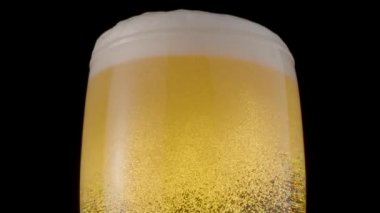 Siyah arka planda bir bardak light bira. Köpük ve köpük yavaşça bira bardağının tepesine tırmanıyor. Saat yönünde döndürme. 