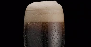 Siyah arka planda bir bardak siyah bira. Bardakta bira sallanıyor, kabarcıklar ve köpük yükseliyor. Bir bardak bira saat yönünde döner..