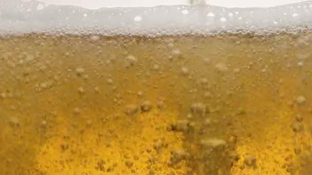 Gros plan sur le contenu d'un verre de bière. La bière est lentement versée dans un verre, causant beaucoup de bulles, de vagues et de mousse.