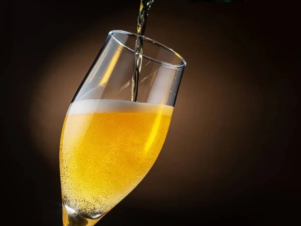 ビールのジェットがビールグラスに注ぎ込まれ 泡や泡がたくさん発生します 暗褐色の背景 — ストック写真