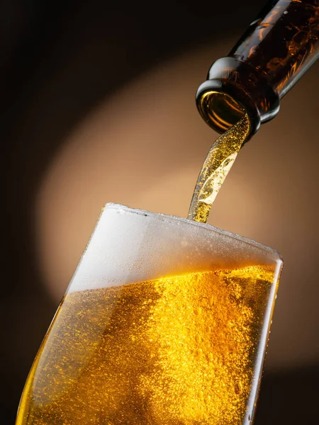 ボトルの外のビールのジェットは 泡や泡の多くを引き起こす ビールグラスに注ぎ込まれます 暗褐色の背景 — ストック写真