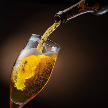 Şişeden çıkan biralar bira bardağına dökülüyor, bu da bir sürü köpüğe ve köpüğe neden oluyor. Koyu kahverengi arkaplan.
