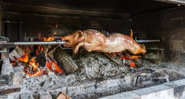 Süt kuzusu domuz, yanan odun sobasının üzerinde tükürük içinde kavruluyor..