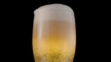 Siyah arka planda bir bardak light bira. Bir jet kadehi yavaşça bira ile doldurarak bol köpük ve kabarcıklara neden olur. Saat yönünde döndürme.