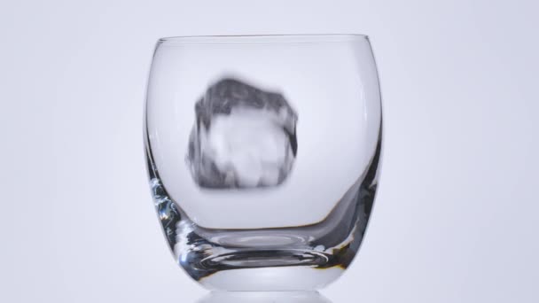 Des cubes de glace tombent lentement dans le verre, puis le whisky ou le rhum est versé. Fond blanc.