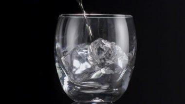 Buz küpleri yavaşça bardağa düşer ve sonra viski ya da rom dökülür. Siyah arkaplan.