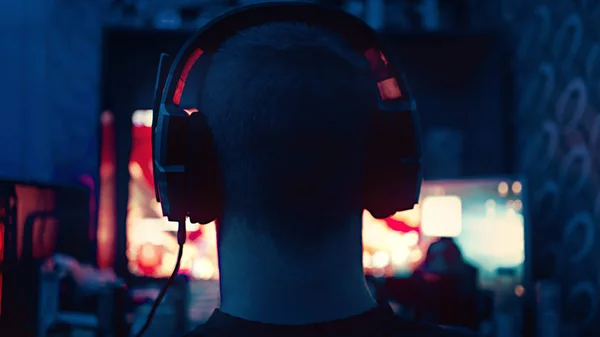 一个游戏玩家坐在一个带耳机的大型监视器前 耳机中的轮廓在一个带着电脑游戏的监视器的背景下 那家伙在家里玩电脑游戏 — 图库照片