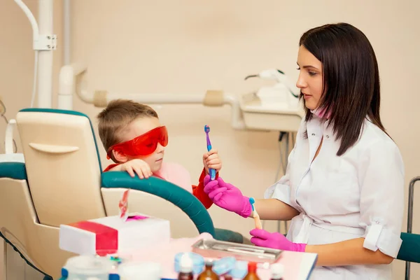 Petit enfant pendant le brossage de ses dents le dentiste au bureau s'assoit avec les enfants et leur apprend à se brosser les dents, les enfants sont heureux — Photo