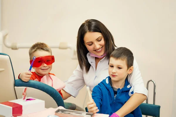Criança pequena durante a escovação de seus denteso dentista no escritório senta-se com as crianças e ensina-lhes como escovar os dentes, as crianças estão felizes — Fotografia de Stock