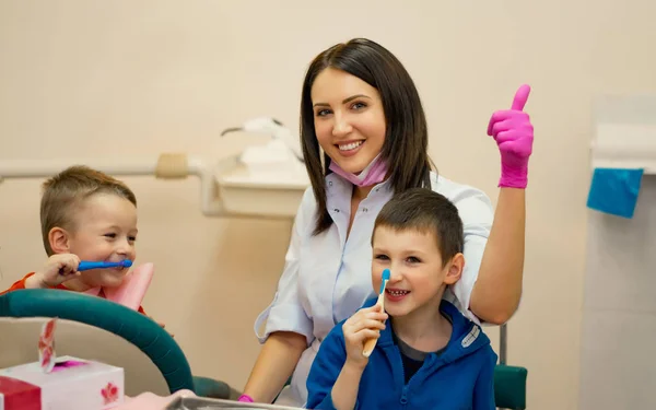 Criança pequena durante a escovação de seus denteso dentista no escritório senta-se com as crianças e ensina-lhes como escovar os dentes, as crianças estão felizes — Fotografia de Stock