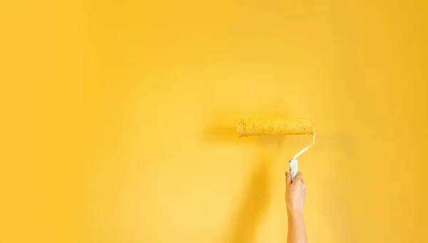 女性の手は黄色の塗装壁の近くに黄色の塗装ローラーを保持します — ストック写真