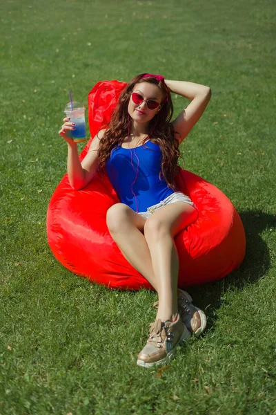 a woman of 25 years of Caucasian appearance, sunbathes in the sun, listens to music, is photographed, she is in blue body and red glasses, the concept of summer vacation