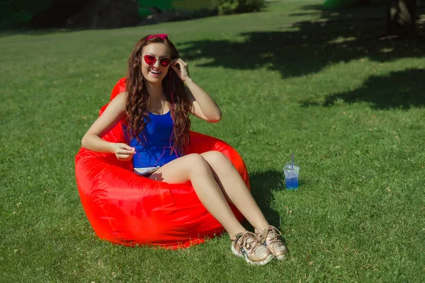 a woman of 25 years of Caucasian appearance, sunbathes in the sun, listens to music, is photographed, she is in blue body and red glasses, the concept of summer vacation