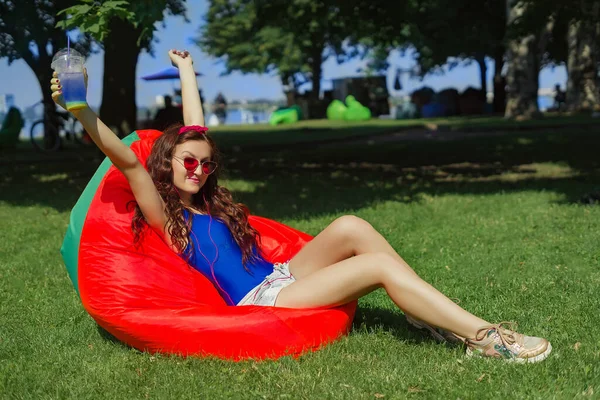 a woman of 25 years of Caucasian appearance, sunbathes in the sun, listens to music, is photographed, she is in blue body and red glasses, the concept of summer vacation