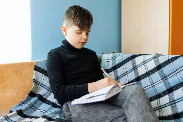 Distance learning online education. A schoolboy studies at home from the phone and does the homework of the school. Training books and notebooks on the table