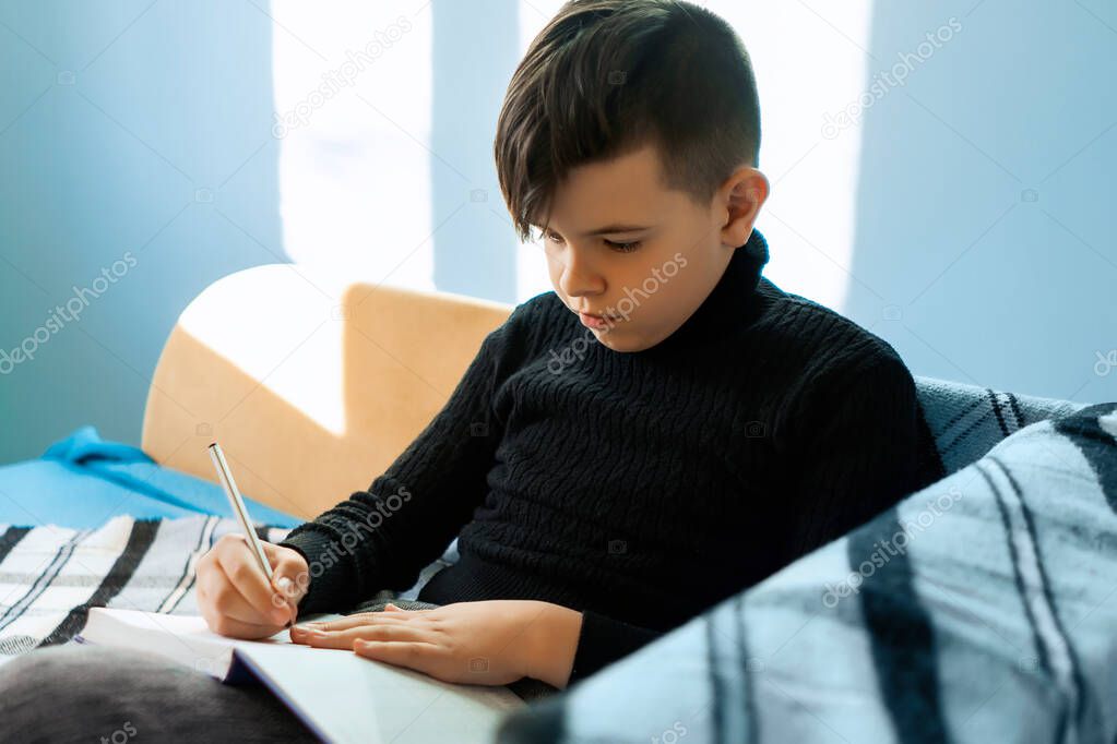Distance learning online education. A schoolboy studies at home from the phone and does the homework of the school. Training books and notebooks on the table