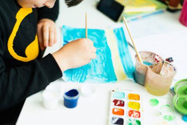 Bebek sanatçısı aksesuarları koleksiyonu. Tuval, suluboya, sanat fırçaları ve beyaz bir masanın üzerinde duran beyaz bir defter. Çocuk sanatçı atölyesi geçmişi.