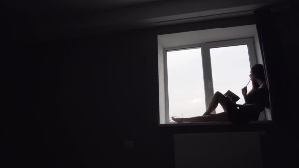 Silueta de chica atractiva sentada en el alféizar de la ventana — Vídeo de stock