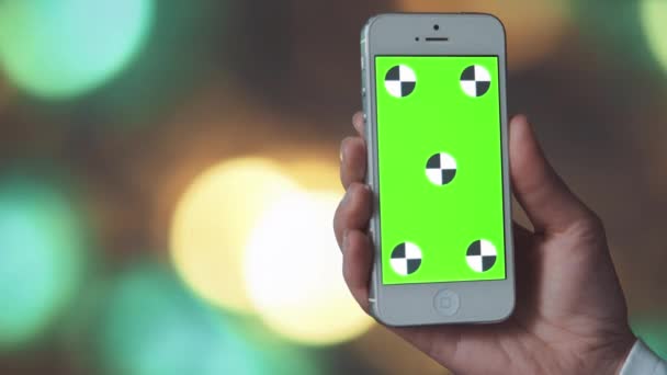 Smartphone mit grünem Bildschirm vor Bokeh-Hintergrund — Stockvideo