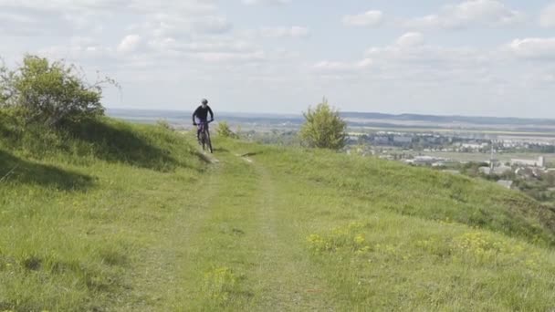 Man rider cykel uppför berget gräs backe — Stockvideo
