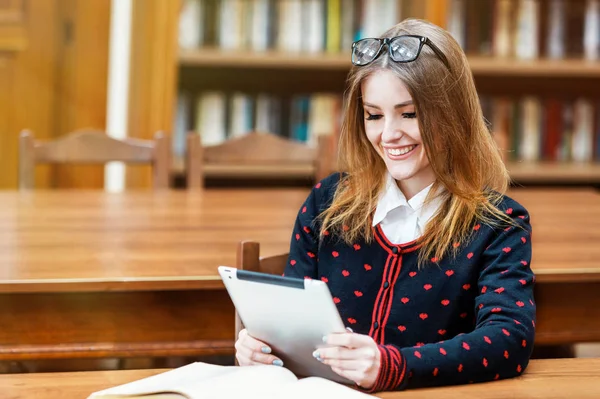 ブロンドの女の子が図書館でタブレットを使用します。 — ストック写真