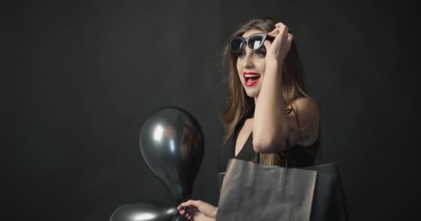 Glimlachende vrouw met zwarte ballonnen en boodschappentas — Stockvideo