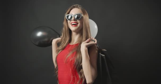 Mujer en vestido rojo sosteniendo bolsas y globos — Vídeos de Stock